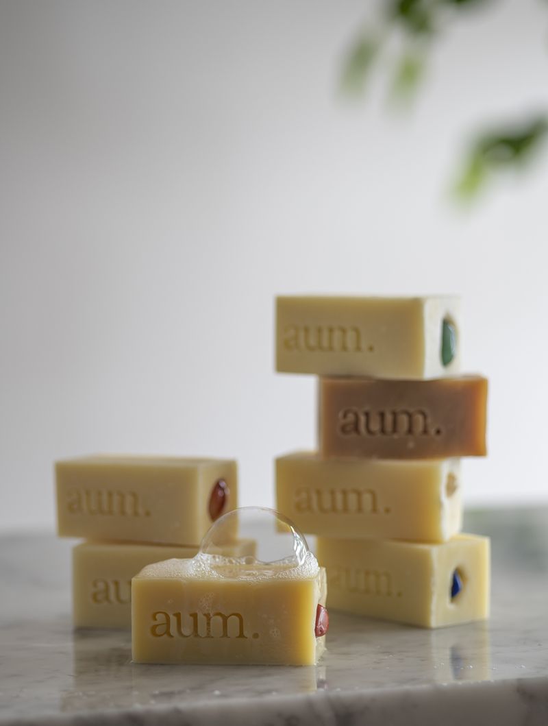 Los siete jabones aum. apilados en dos torres sobre superficie de mármol, bokeh botánico al fondo