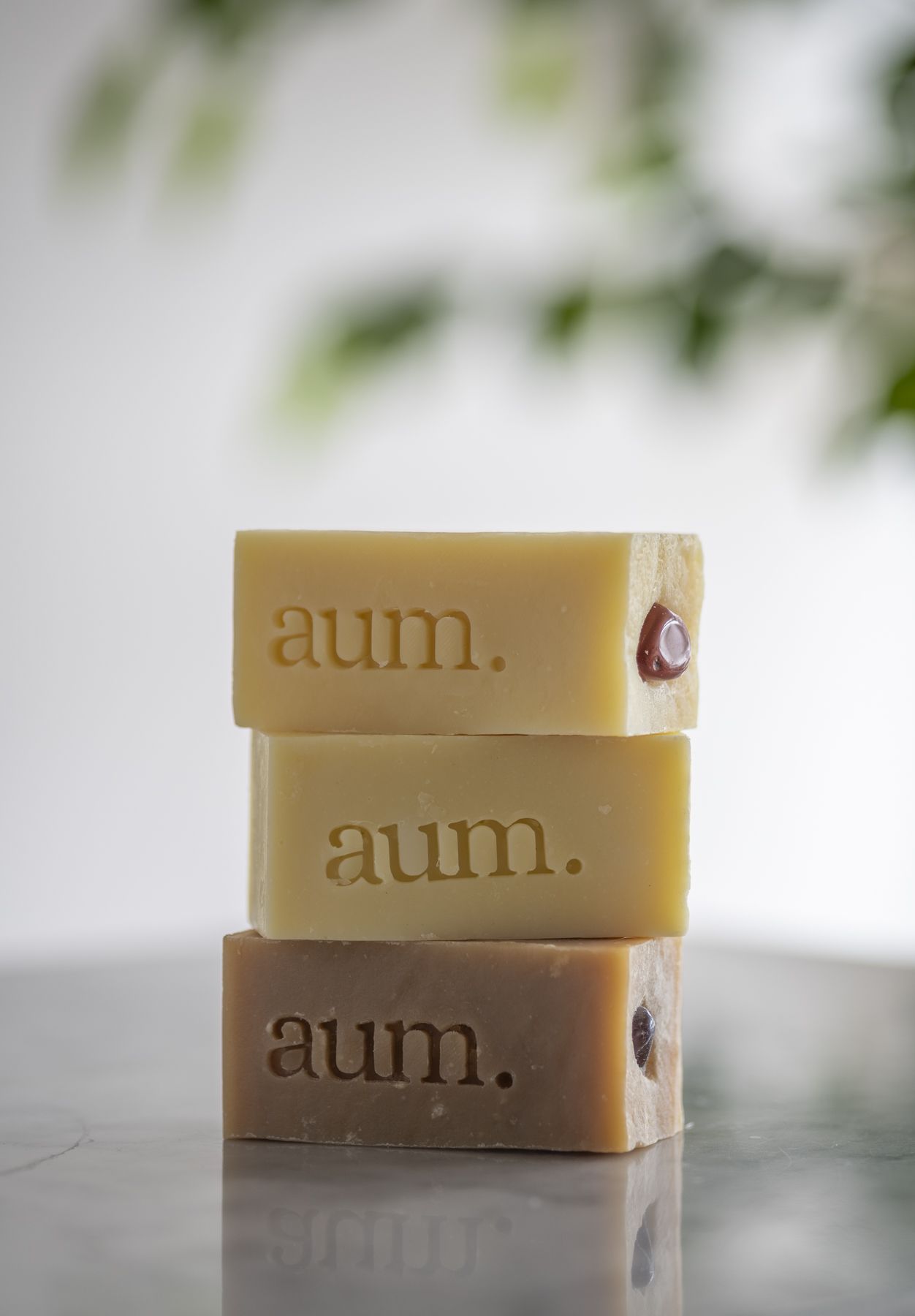 Tres jabones aum. apilados sobre superficie de mármol con bokeh botánico