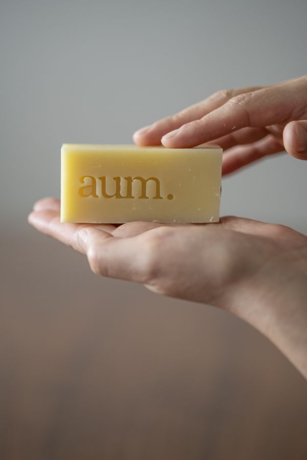 Mano sosteniendo una barra de jabón aum. con espuma, fondo gris neutro